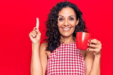 Orta yaşlı, güzel bir kadın kahve fincanı içerken bir fikirle gülümsüyor ya da bir soru işareti yapıyor. 