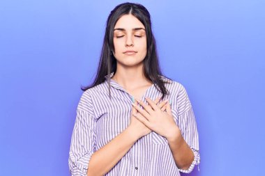 Sıradan çizgili tişört giyen, elleri göğsünde gülümseyen, gözleri kapalı, yüzünde minnet ifadesi olan genç ve güzel bir kız. sağlık kavramı. 