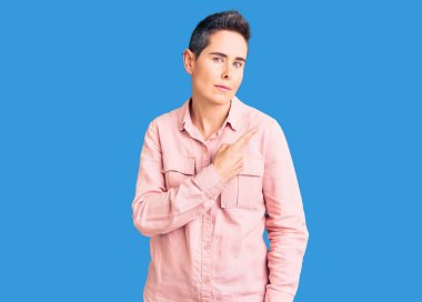 Kısa saçlı, günlük giysiler giyen, el parmaklarıyla kenarı gösteren genç bir kadın, ciddi ve sakin bir yüz ifadesi sergiliyor. 