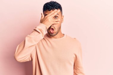 Gündelik kıyafetler giyen genç İspanyol adam şok içinde yüzünü ve gözlerini eliyle kapatıyor, parmaklarından korkuyla bakıyor. 