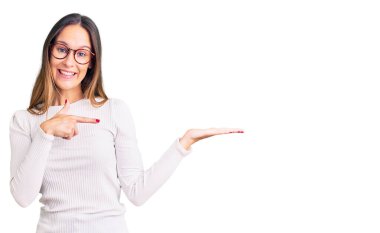 Güzel esmer, beyaz süveter giyen, gözlüklü genç bir kadın kameraya hayret ediyor ve gülümsüyor.. 