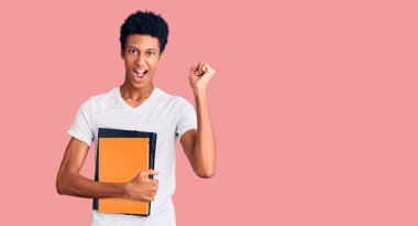 Genç Afrikalı Amerikalı adam elinde kitapla gururla bağırıyor zaferi ve başarıyı kutluyor. 