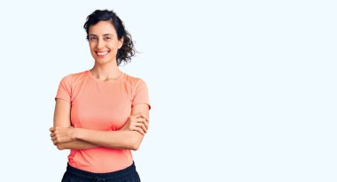 Spor kıyafetleri giyen, kollarını kavuşturup kameraya gülümseyen güzel İspanyol bir kadın. pozitif kişi. 