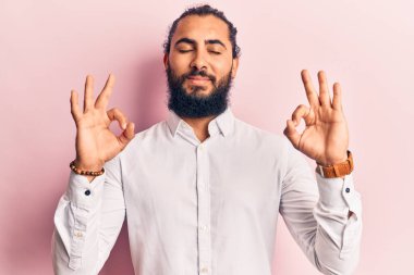 Gündelik kıyafetler giyen genç Arap adam rahatla ve gözleri kapalı gülümse parmaklarıyla meditasyon hareketi yapıyor. yoga konsepti. 