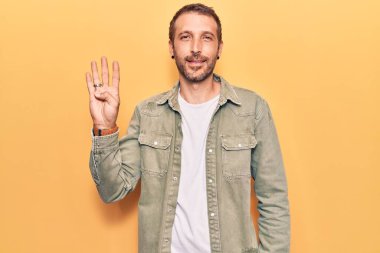 Genç, yakışıklı, günlük kıyafetler giyen, dört numarayı gösteren ve gülümseyen, kendinden emin ve mutlu bir adam.. 