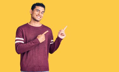 İspanyol asıllı yakışıklı, sıradan kıyafetler giyen, gülümseyen ve kameraya bakan iki eli ve parmakları yanda olan genç bir adam.. 