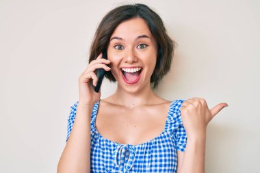 Genç, güzel bir kız akıllı telefondan konuşuyor. Parmağını kaldırıyor, gülümsüyor, ağzı açık. 