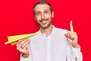 Elinde kağıt uçak tutan genç yakışıklı bir adam bir fikirle gülümsüyor ya da bir soru işareti yapıyor mutlu bir yüzle, bir numara 