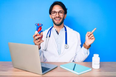 Yakışıklı, doktor üniforması giyen, kalbi tutan, gülümseyen, elleri ve parmakları yandan gösteren İspanyol bir adam. 