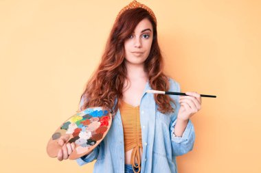 Elinde boya fırçası ve palet tutan genç ve güzel bir kadın. Düşünce tarzı ve ayık bir yüz ifadesi. Kendine güvenen biri. 