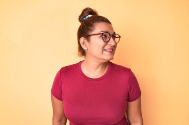 Orta yaşlı esmer, günlük kıyafetler ve gözlük takan, rahat profil pozu veren, kendine güvenen, gülümseyen İspanyol kadın.. 