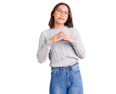 Genç, güzel Çinli kız, sıradan kıyafetler giyip ellerini birleştiriyor ve gülümsüyor. Rahat ve neşeli. Başarı ve iyimserlik 