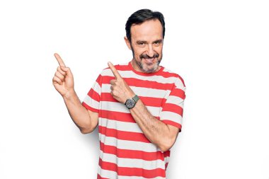 Orta yaşlı, çizgili tişört giyen yakışıklı adam izole edilmiş beyaz arka planda duruyor gülümsüyor ve kameraya bakıyor iki eliyle ve parmaklarıyla yan tarafa bakıyor..