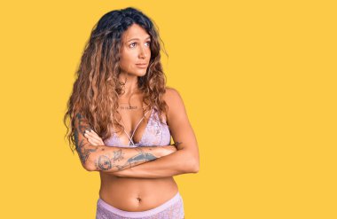 Dövmeli, iç çamaşırlı, kolları çapraz ve kendinden emin bir kadın. 