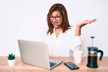 Orta yaşlı esmer kadın ofiste çalışan operatör kulaklığı takıyor zaferi mutlu bir gülümsemeyle kutluyor ve kazanan ifade ellerini kaldırıyor. 