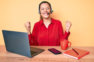 Çağrı merkezinde operatör kulaklığı takan genç esmer kadın çok mutlu ve heyecanlı bir şekilde kolları havada, gülümseyerek ve başarı için bağırarak kazanan jestler yapıyor. kutlama konsepti. 