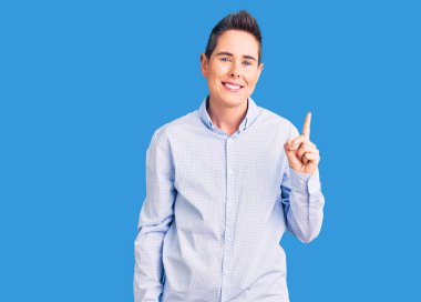 Kısa saçlı, iş kıyafetleri giyen genç bir kadın bir numarayı gösterip işaret ederken kendinden emin ve mutlu bir şekilde gülümsüyor.. 