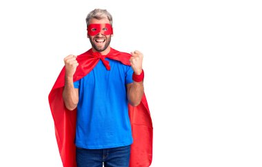 Sarışın, süper kahraman kıyafeti giymiş genç bir adam kollarını kaldırıp, gözlerini açarak başarının şaşkınlığını ve şaşkınlığını kutluyor. Kazanan konsept. 