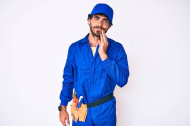 Kıvırcık saçlı ve ayı gibi giyinen yakışıklı genç adam diş ağrısı ya da diş ağrısı yüzünden elleriyle dudaklarına dokunuyor. dişçi 