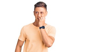 Günlük kıyafetler giyen genç yakışıklı adam gergin ve gergin görünüyor. Ağzı tırnak yiyen eller. anksiyete. 