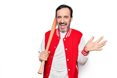 Orta yaşlı yakışıklı sporcu ceketi giyen beysbol oynayan ahşap sopa kullanan mutlu bir gülümsemeyle başarıyı kutlayan ve elini kaldıran bir adam.