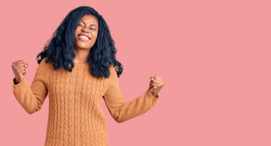 Güzel afro-amerikan kadını kolları havada ve gözleri kapalı zaferi kutlarken rahat bir süveter giyer. Kazanan konsept. 