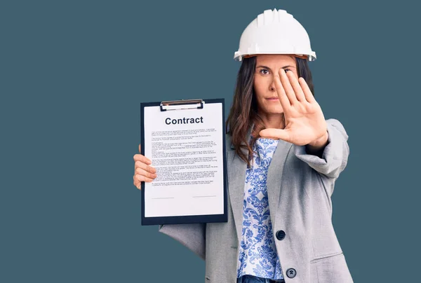 Young Beautiful Brunette Woman Wearing Architect Hardhat Holding Contract Open — Stock Photo, Image