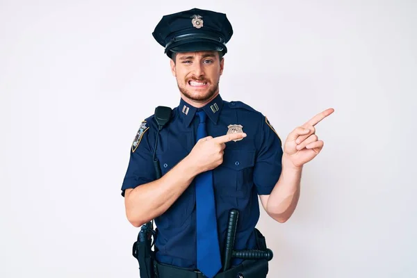 Young caucasian man wearing police uniform pointing aside worried and nervous with both hands, concerned and surprised expression