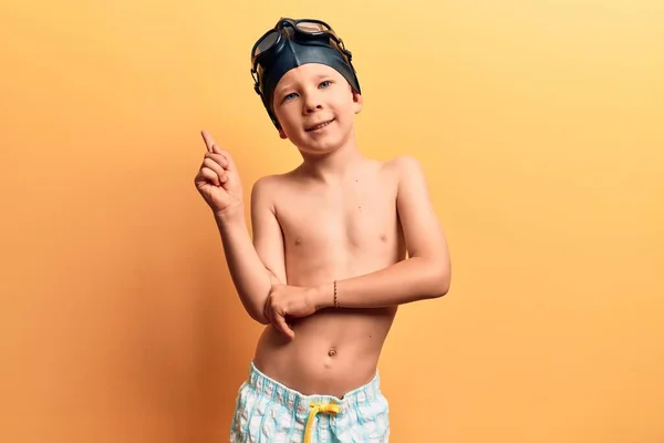 可爱的金发碧眼的孩子穿着泳衣 戴着泳镜 高兴地微笑着 手指头指向旁边 — 图库照片