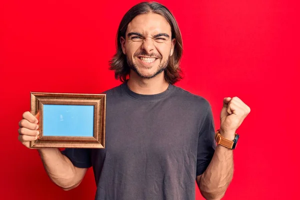 Joven Hombre Guapo Sosteniendo Marco Vacío Gritando Orgulloso Celebrando Victoria — Foto de Stock