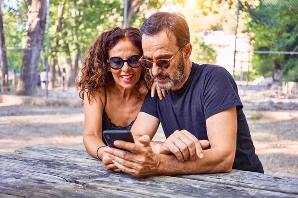 Pareja Mediana Edad Sonriendo Feliz Con Teléfono Inteligente Sentado Banco —  Fotos de Stock