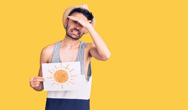 Young hispanic man wearing summer hat holding sun draw stressed and frustrated with hand on head, surprised and angry face