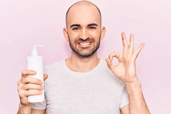 Joven Hombre Calvo Guapo Sosteniendo Botella Crema Loción Haciendo Signo — Foto de Stock