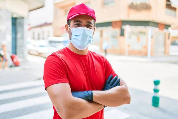 街の通りに立って制服やコロナウイルス対策医療マスクを身に着けている若い配達人 — ストック写真