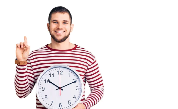 Jovem Homem Bonito Segurando Relógio Grande Surpreso Com Uma Ideia — Fotografia de Stock