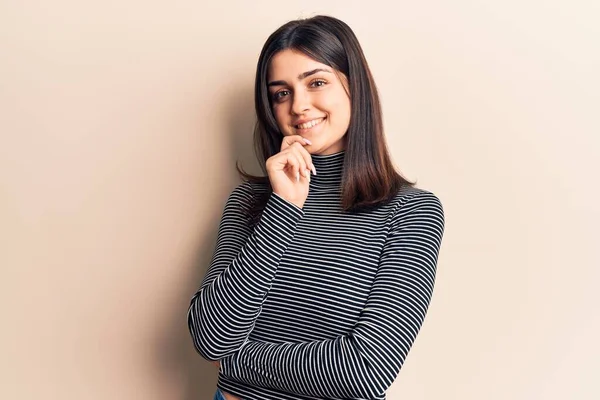 Young beautiful girl wearing casual striped t shirt smiling looking confident at the camera with crossed arms and hand on chin. thinking positive.