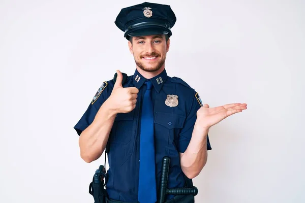 Young caucasian man wearing police uniform showing palm hand and doing ok gesture with thumbs up, smiling happy and cheerful