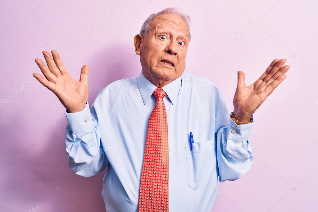 Senior handsome grey-haired businessman wearing elegant tie standing over pink background clueless and confused with open arms, no idea and doubtful face.