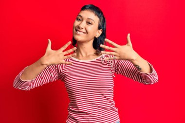 Günlük kıyafetler giyen genç bir kadın on numarayı gösterip işaret ederken kendinden emin ve mutlu bir şekilde gülümsüyor.. 