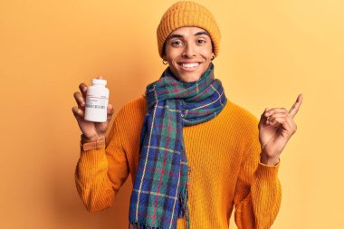 Kışlık giysiler giyen genç Afrikalı Amerikalı adam elinde haplarla mutlu bir şekilde gülümsüyor. 