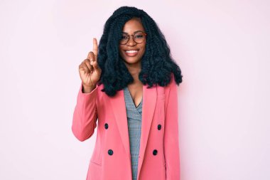 İş ceketi ve gözlük takan güzel Afrikalı kadın bir numaralı parmağını gösterip işaret ederken kendinden emin ve mutlu bir şekilde gülümsüyor.. 