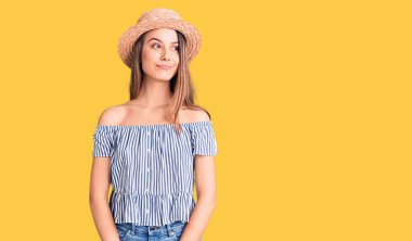 Şapka ve tişört giyen güzel bir kız gülümsüyor, yan tarafa bakıyor ve düşünüyor.. 