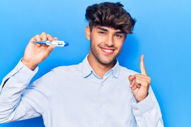 Genç İspanyol adam termometreyi tutarken gülümsüyor. 