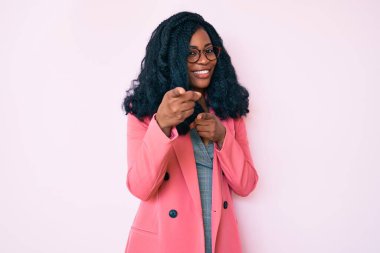 İş ceketi giyen ve gözlüklü güzel bir Afrikalı kadın kamerayı mutlu ve komik yüzüyle işaret ediyor. iyi enerji ve titreşimler. 