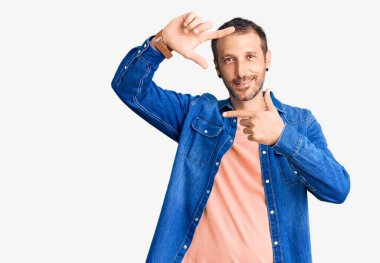 Gündelik kıyafetler giyen, gülümseyen, elleri ve parmakları gülen yüzlü genç yakışıklı bir adam. yaratıcılık ve fotoğrafçılık kavramı. 