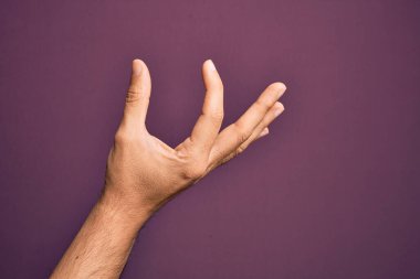İzole edilmiş mor arka plan üzerinde parmaklarını gösteren beyaz bir adamın eli. Görünmez bir şeyi alıyor, parmakları boşluğu gösteren bir nesneyi tutuyor.