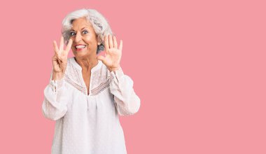 Yaşlı, gri saçlı, günlük kıyafetler giyen, 8 numaralı parmaklarıyla işaret eden, kendinden emin ve mutlu bir kadın.. 