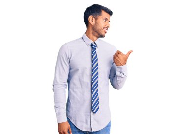 İş elbiseleri giyen, gülen, gülen yüzlü genç latin adam başparmağıyla yan tarafı işaret ediyor.. 