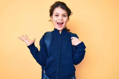 Sevimli İspanyol çocuk sırt çantasını tutuyor zaferi mutlu bir gülümsemeyle ve kazanan yüz ifadesiyle kutluyor. 