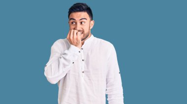 Günlük kıyafetler giyen genç yakışıklı adam gergin ve gergin görünüyor. Ağzı tırnak yiyen eller. anksiyete. 